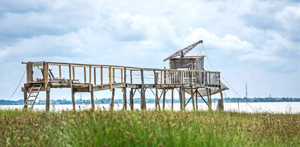 Un carrelet de pêche sur pilotis au bord de l'estuaire, sous un ciel nuageux
